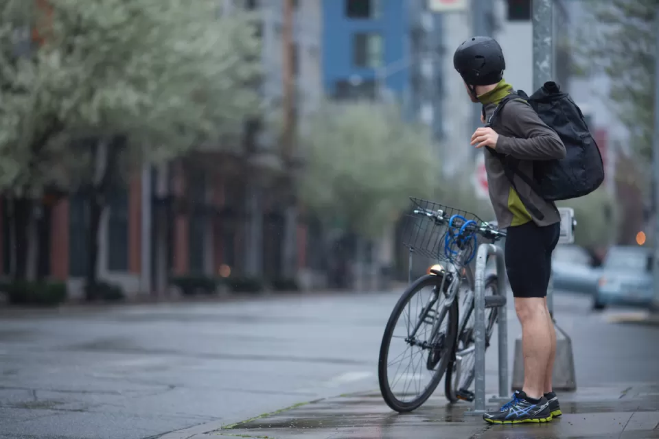 An adult man, stopped on a Seattle, Washington street corner, preparing for a rainy morning bike commute.